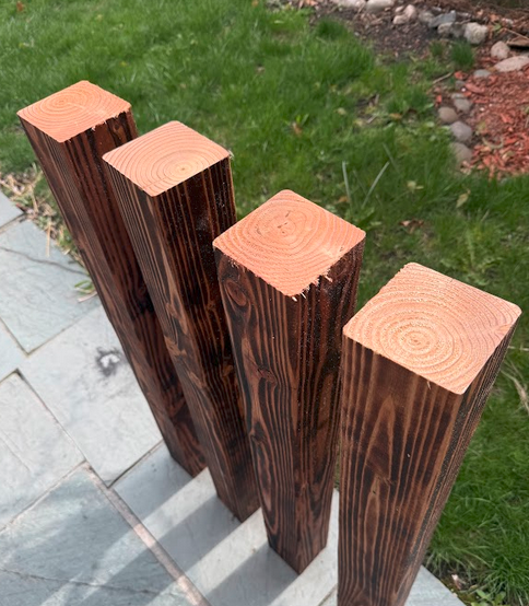 All four finished yakisugi 4×4 legs standing upright, cut to height, end grain visible